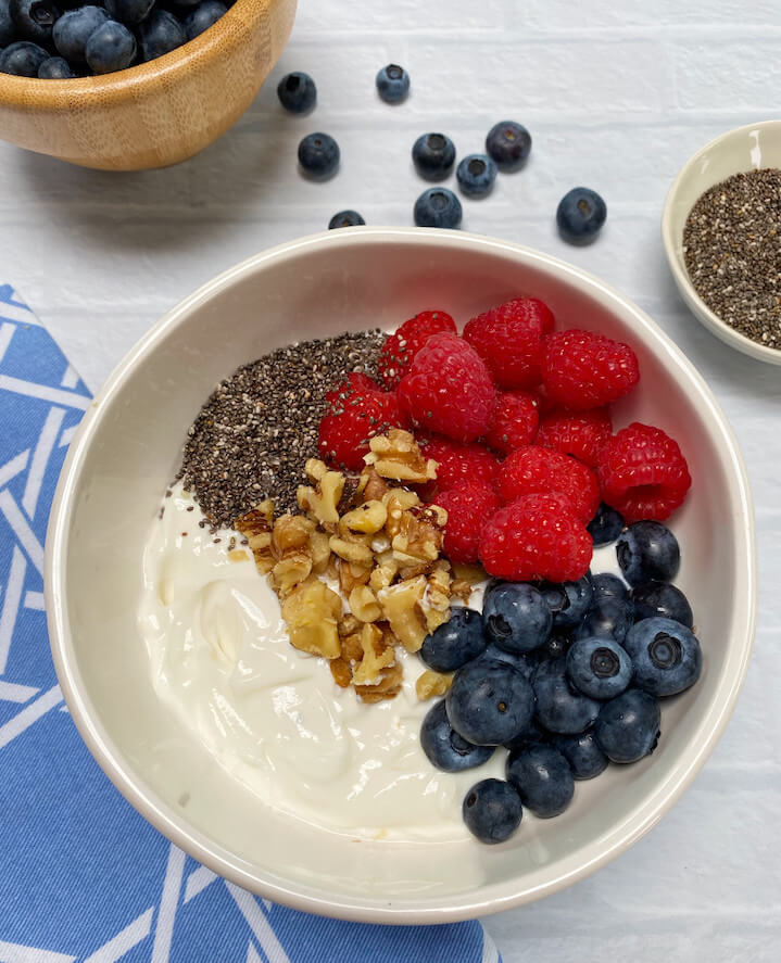 bowl of yogurt topped with walnuts, raspberries, blueberries and chia seeds