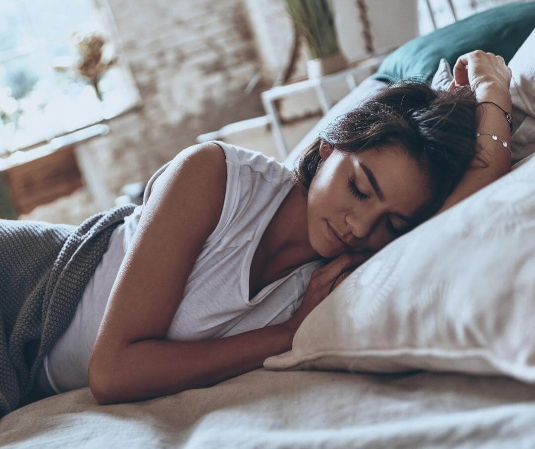 woman sleeping on her side in a well-lit bedroom