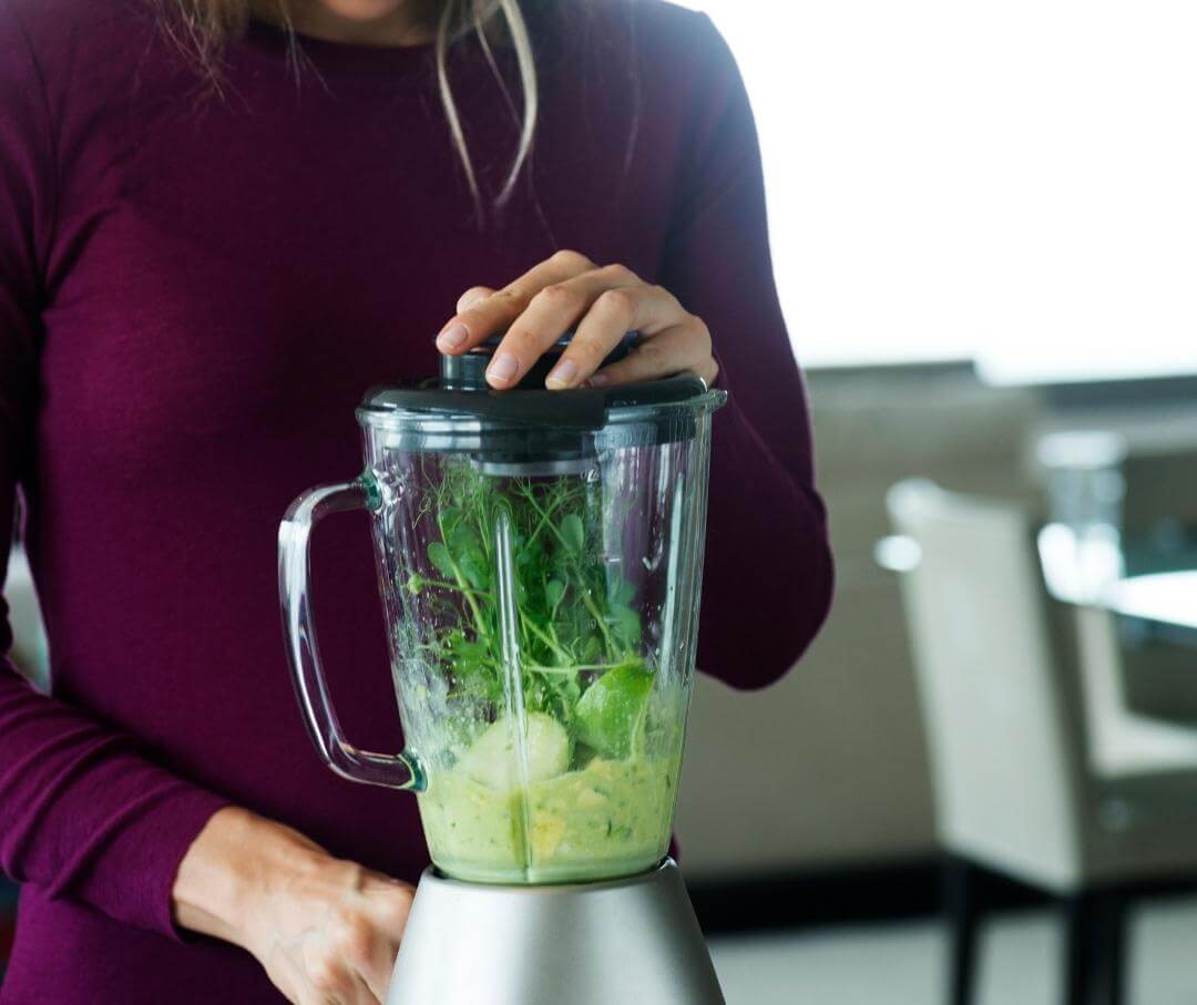 woman mixing green vegetables in a blender