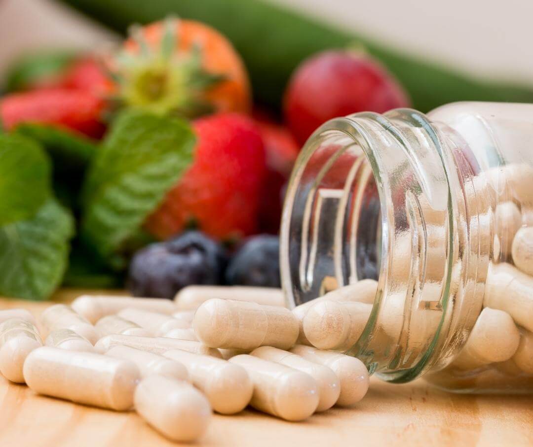 mason jar on its side with vitamin pills, with strawberries and blueberries in the background