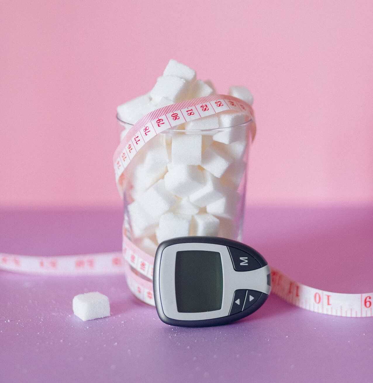 Sugar-Cubes-in-a-Glass-with-measuring-tape-and-glucose-monitor