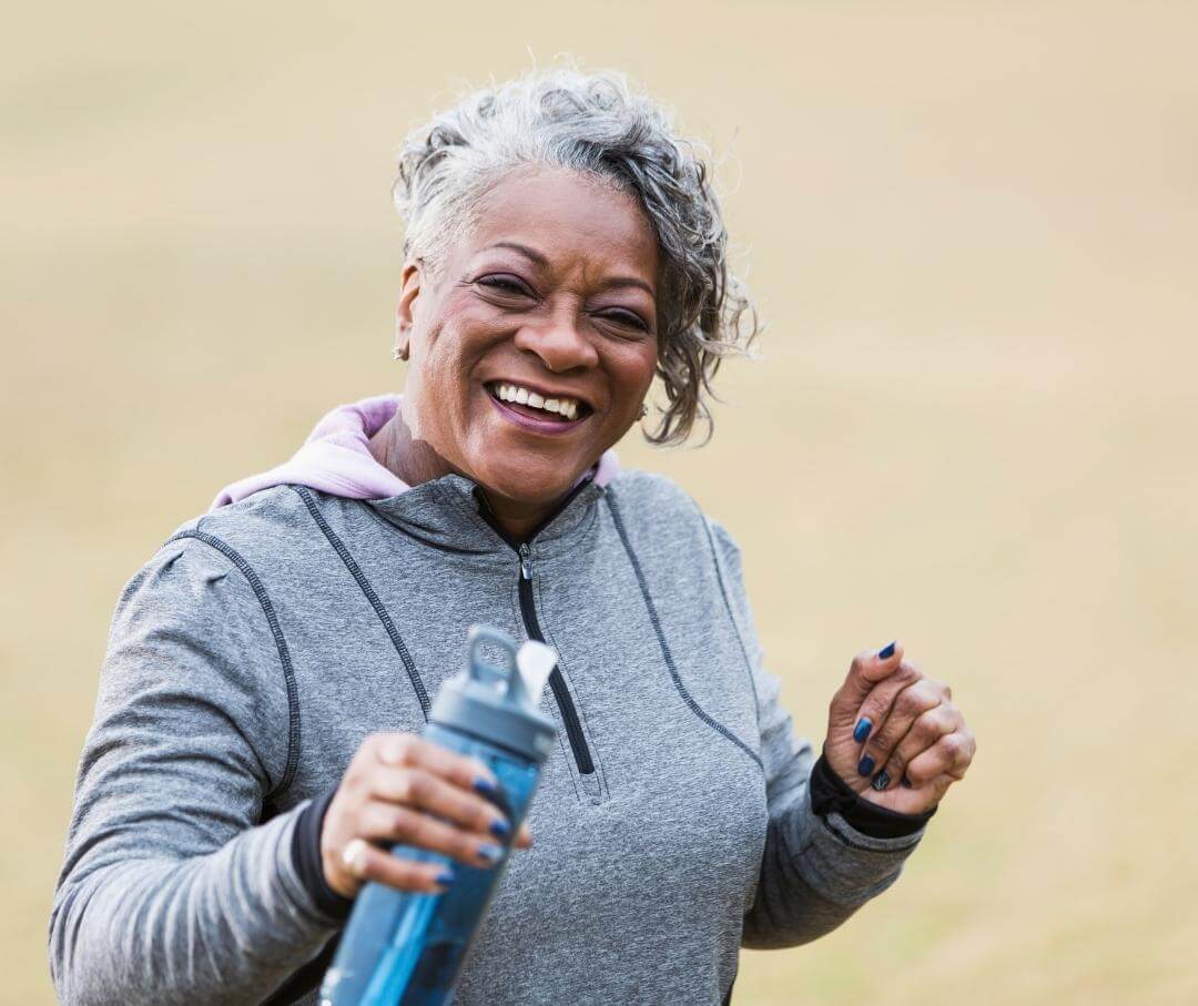 smiling woman wearing workout clothes holding a water bottle