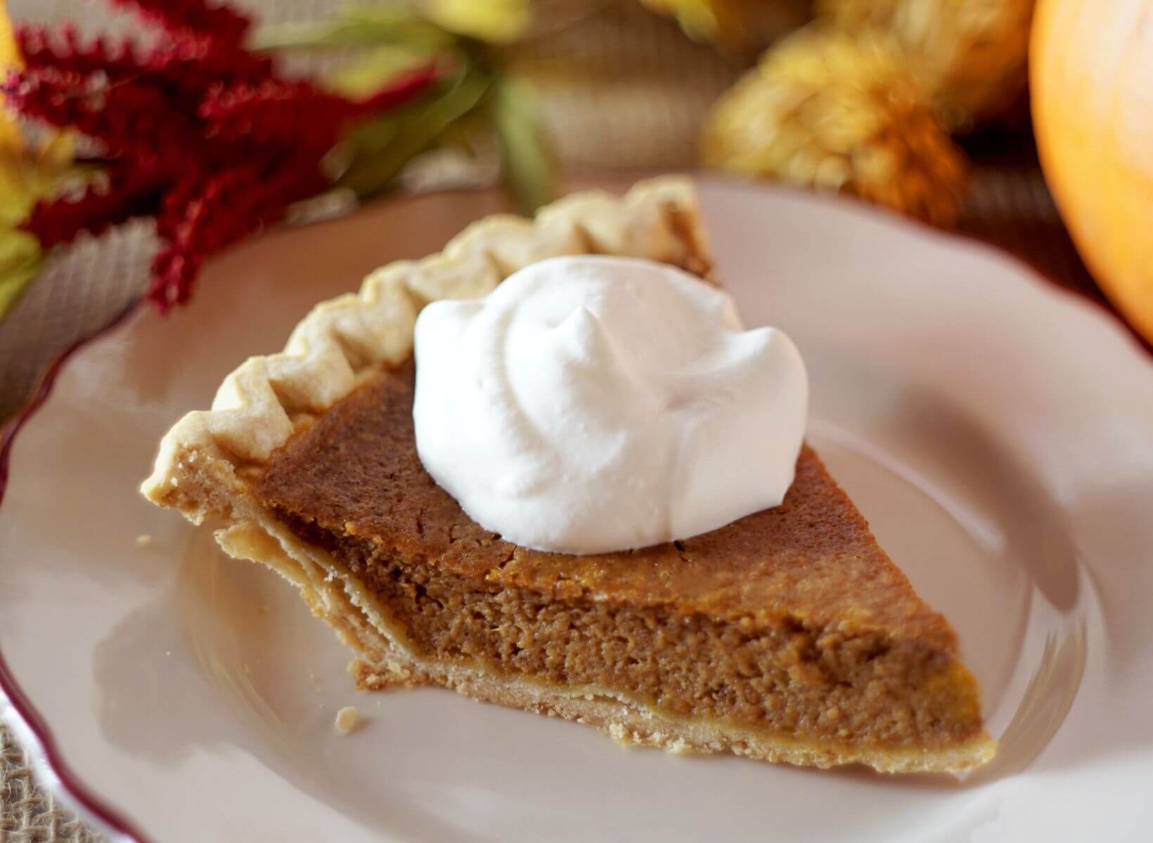 A close up shot of a low-glycemic pumpkin pie slice topped with whipped cream