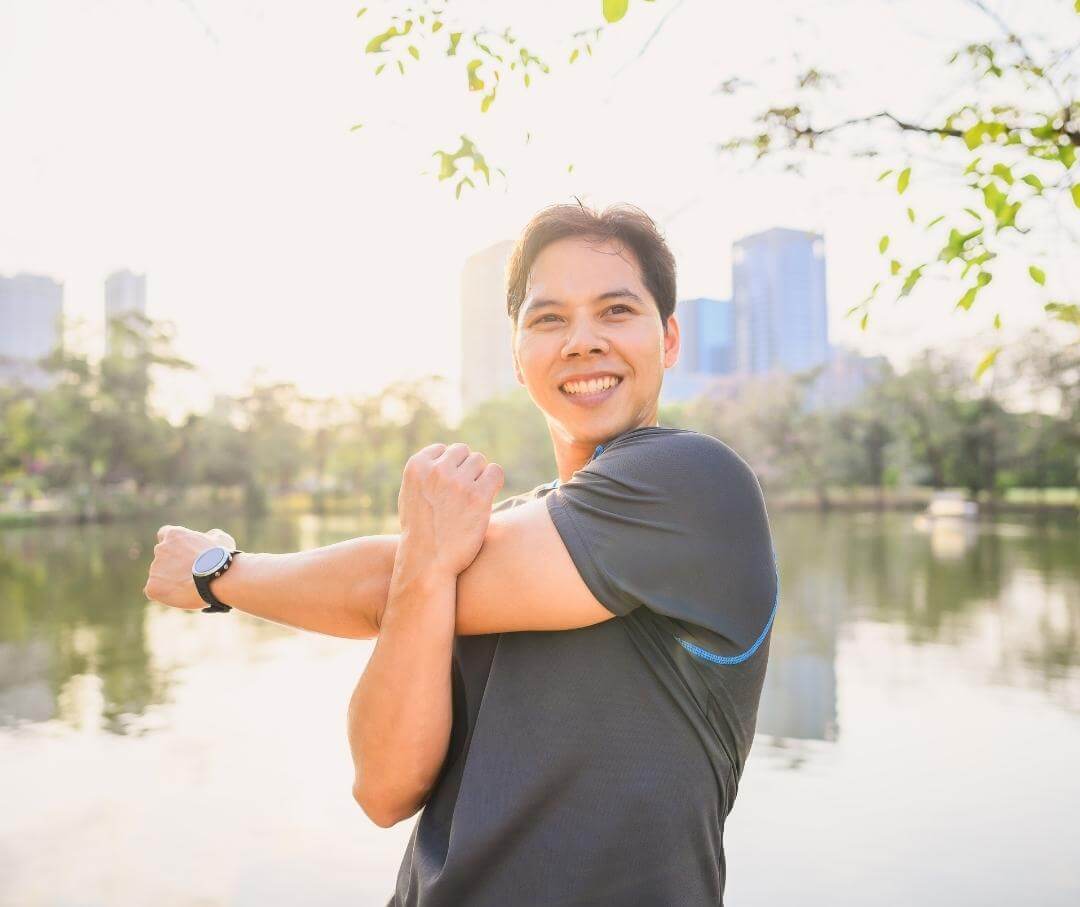 man in a city park smiling and stretching one shoulder