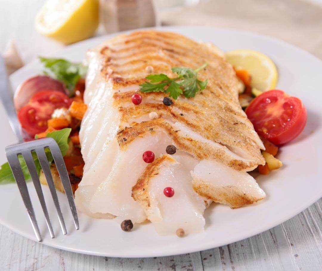 white plate with a baked fish fillet and vegetables