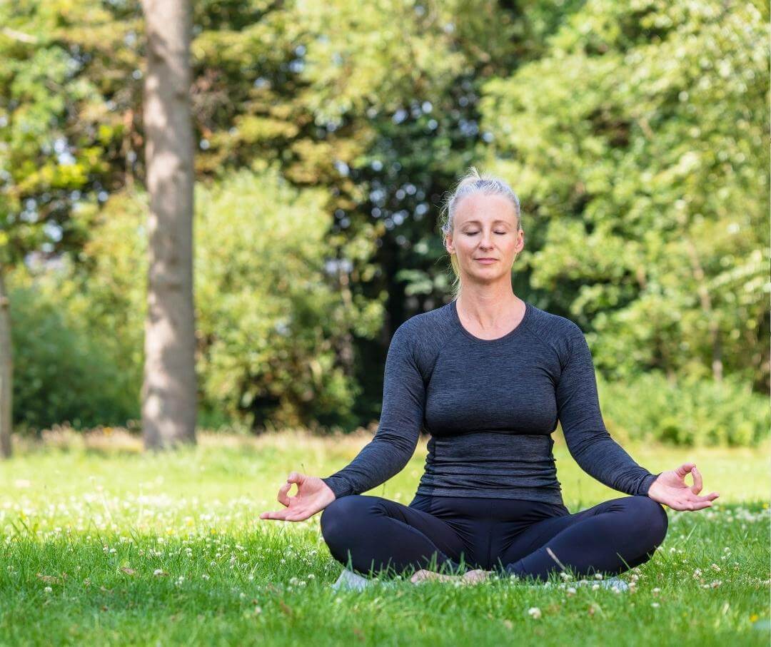 woman with grey hair sitting cross-legged in a meditative pose outdoors