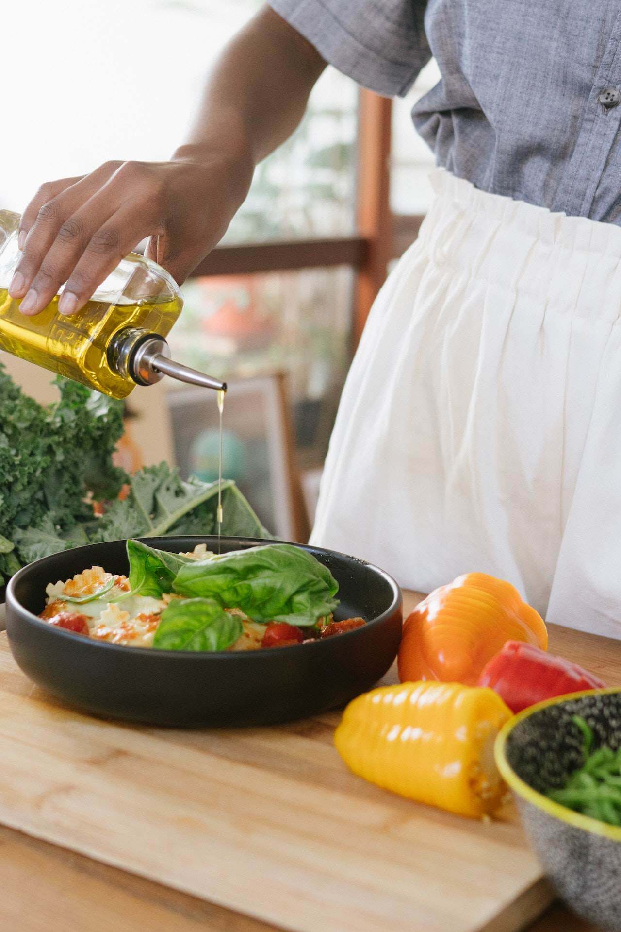 woman-adding-olive-oil-to-vegetables-on-bowl