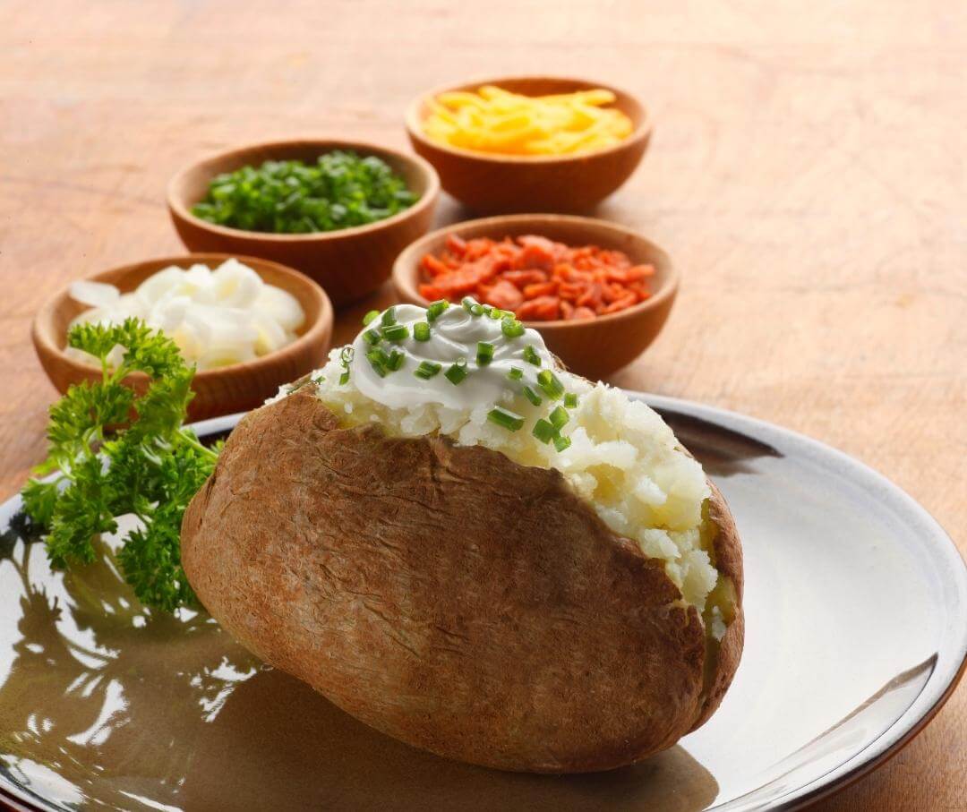 a baked potato alongside several dishes of toppings