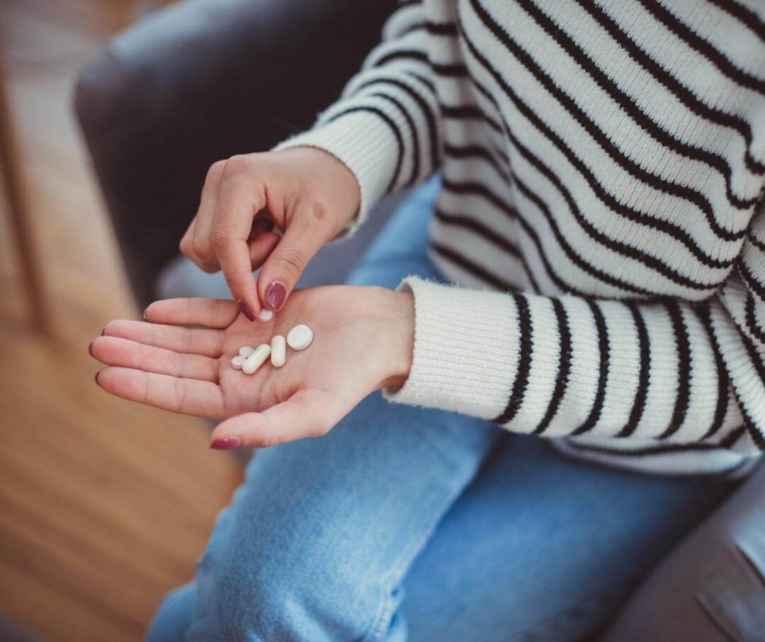 a woman holding a variety of pills in the palm of her hand