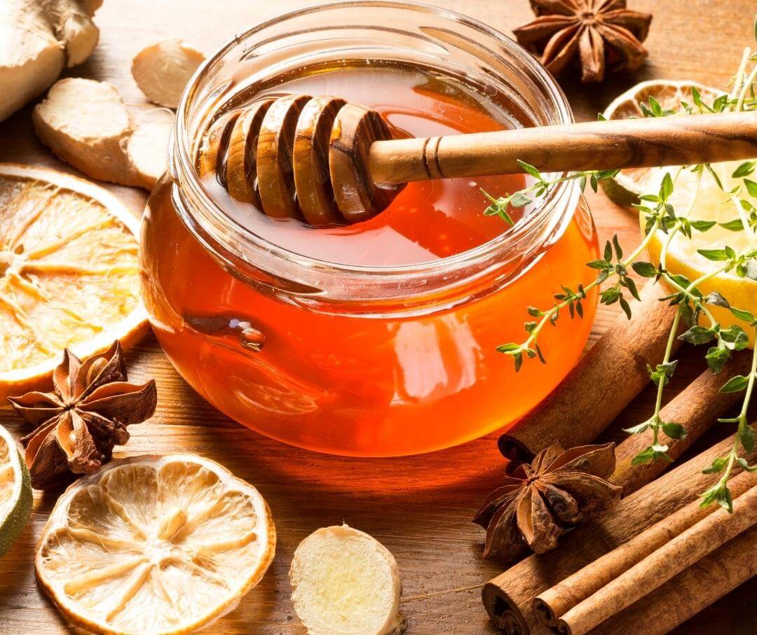 a jar of honey with a wand in it and herbs and spices on the table next to it