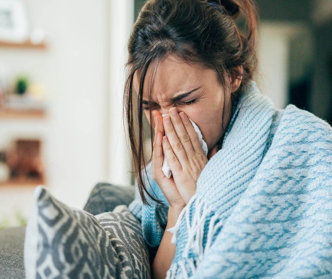 woman wrapped in a blanket blowing her nose