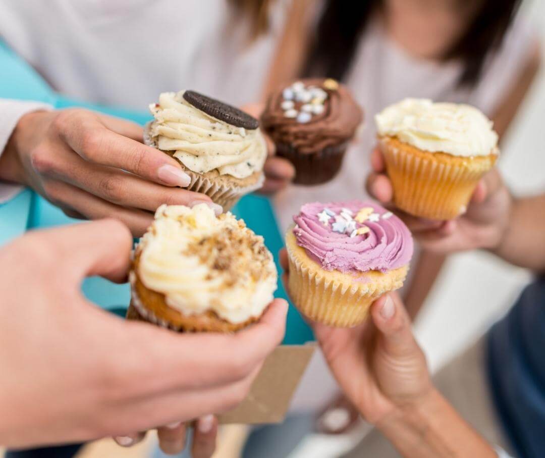 close-up of five hands, each holding a cupcake