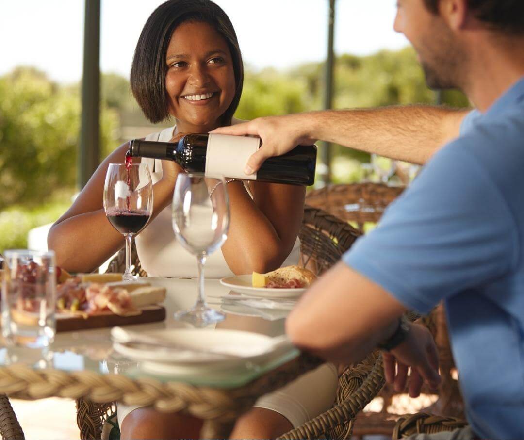 man pouring red wine for woman at dinner table