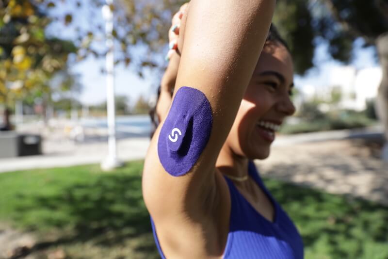 Woman smiling and wearing a CGM plus Signos sport cover on her left tricep