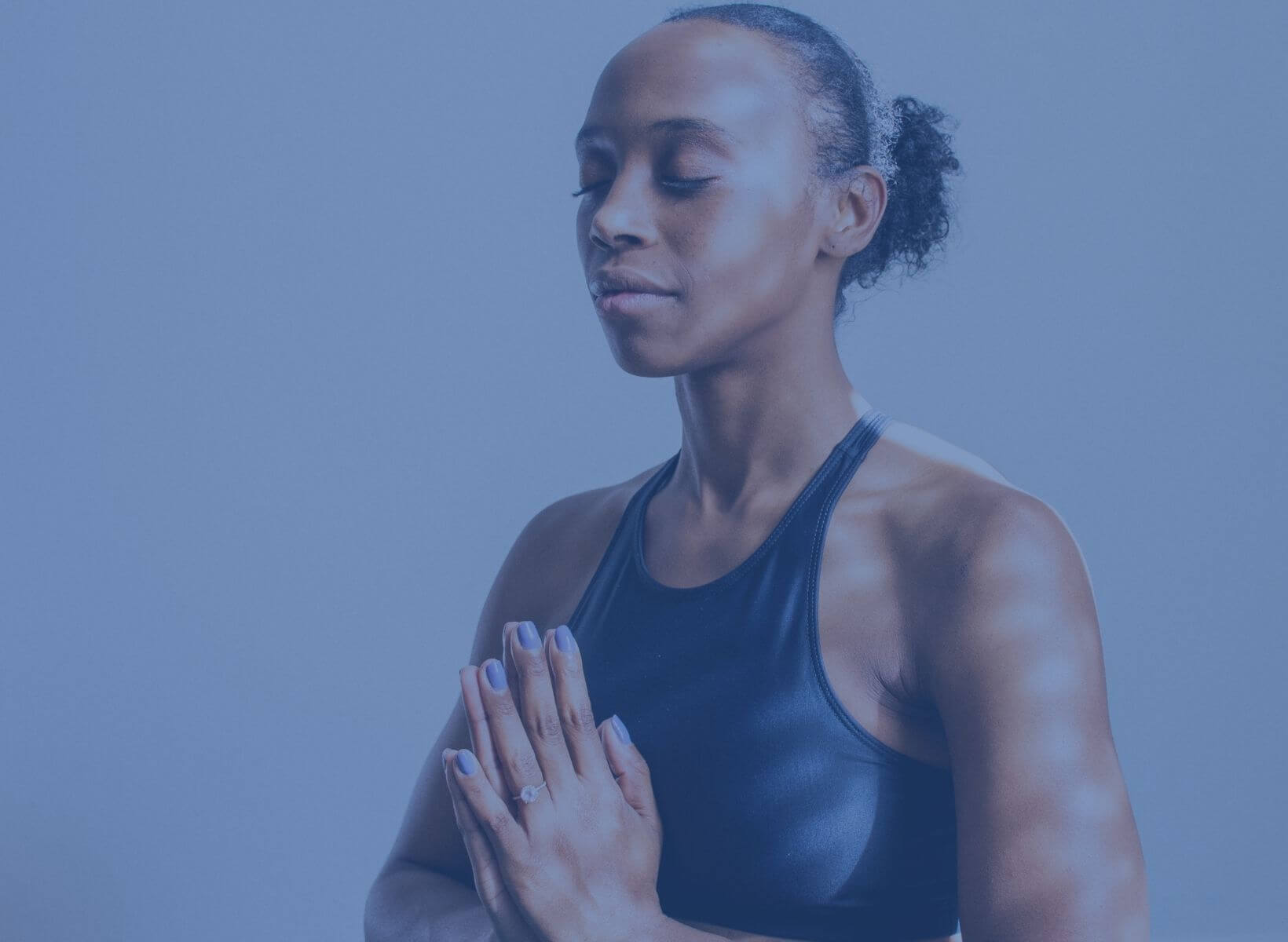 A black woman meditating with her eyes closed and her hands in prayer position in front of her chest