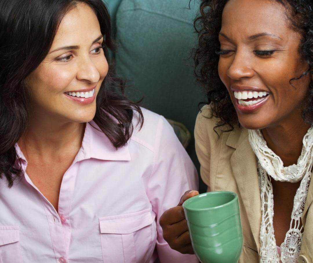 two women sitting next to each other talking and smiling