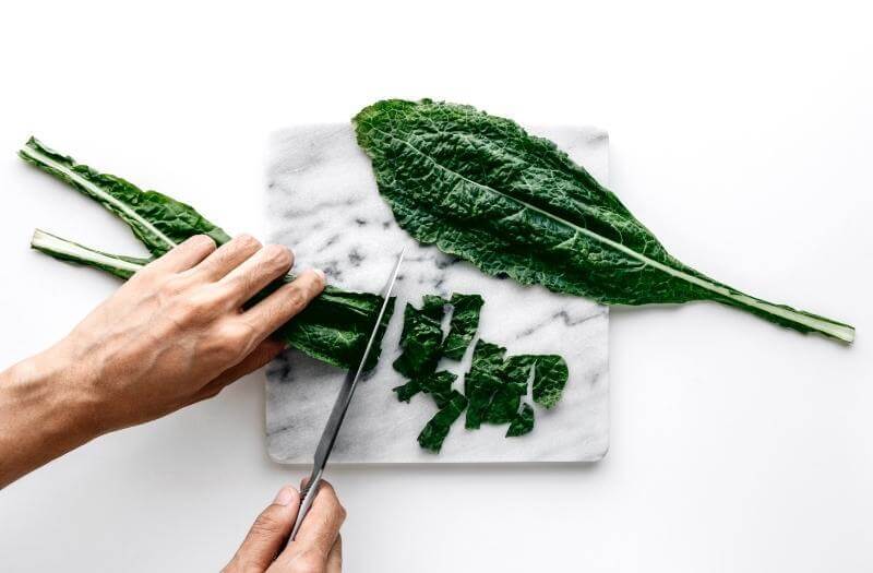 Person chopping kale on a marble cutting board over a white table