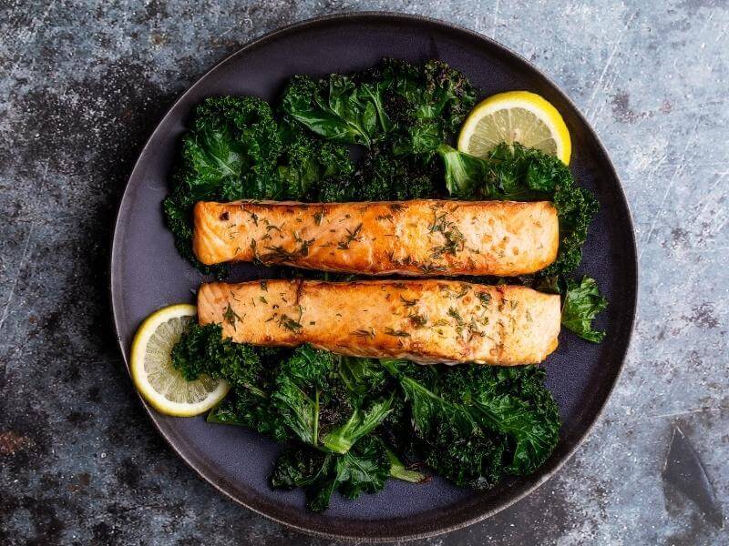 Mediterranean meal with salmon over a bed of kale on a black plate