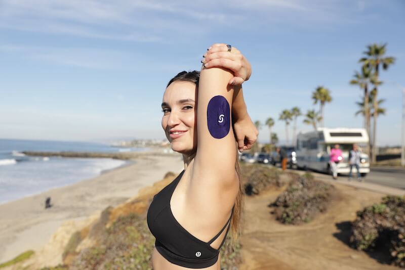 Woman at beach wearing a CGM plus Signos sport cover on her right tricep