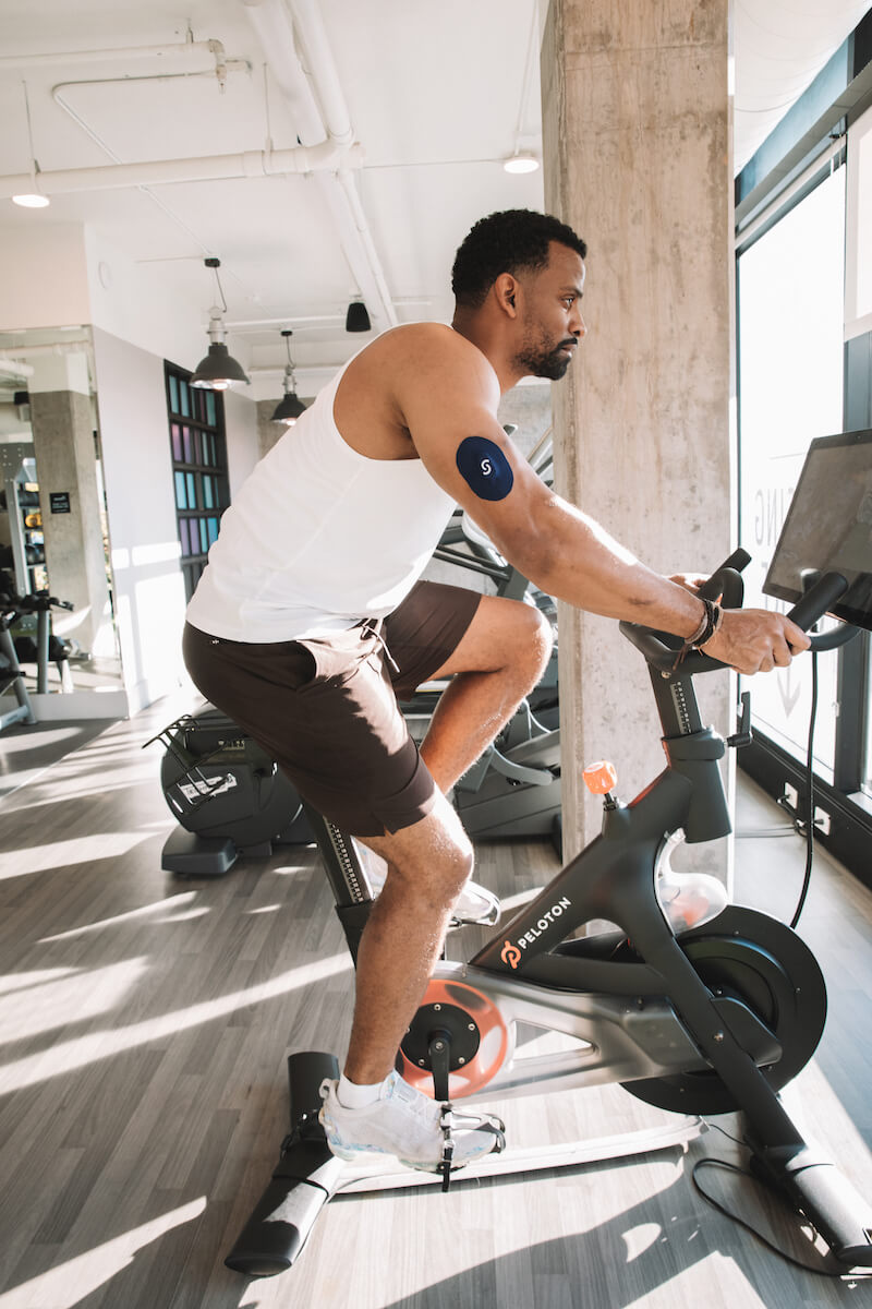 Man riding spin bike while wearing a CGM plus Signos sport cover on his right tricep