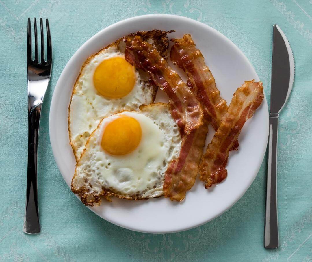 a plate with two fried eggs and three strips of bacon