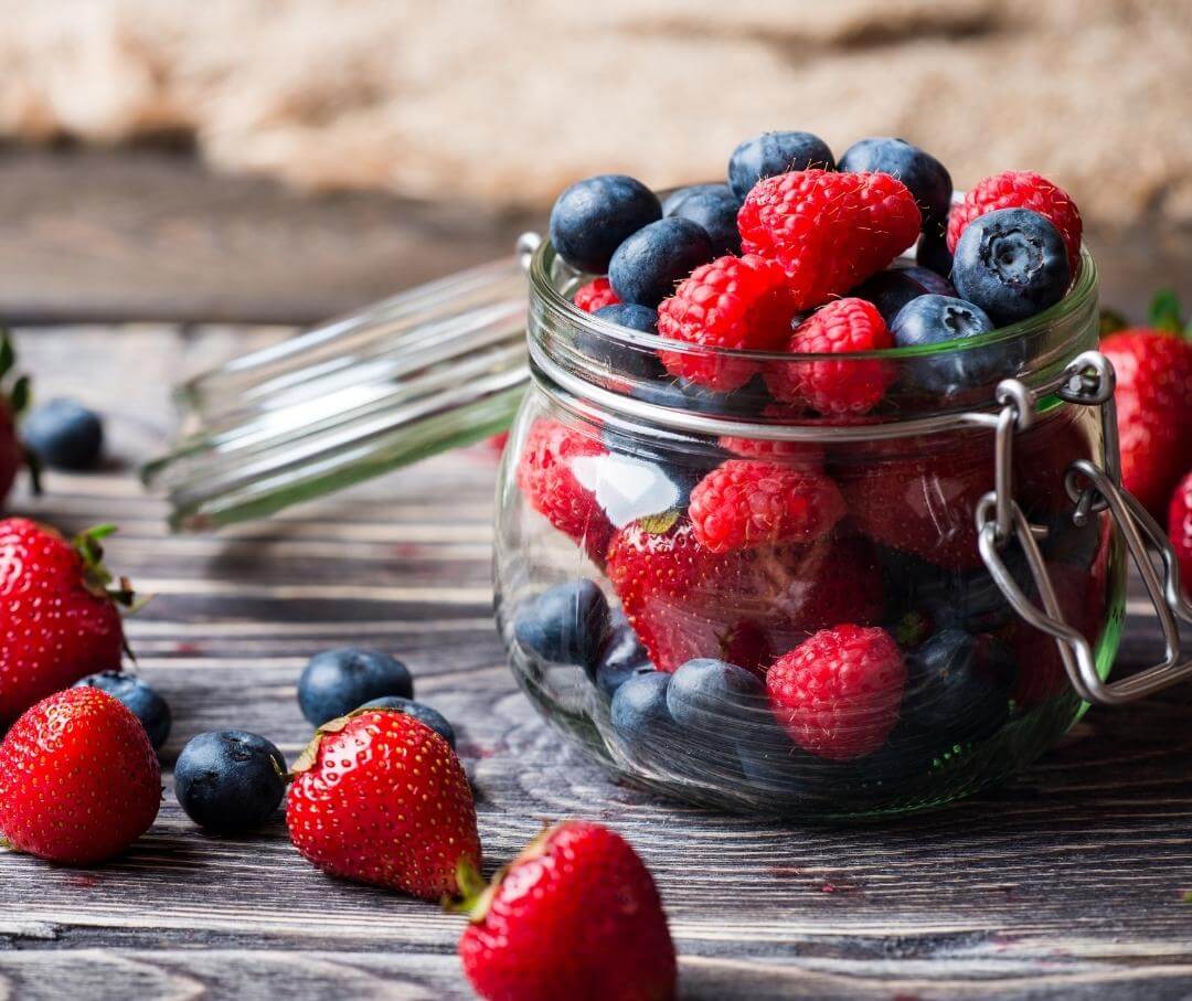 a glass jar filled with strawberries, blueberries and raspberries