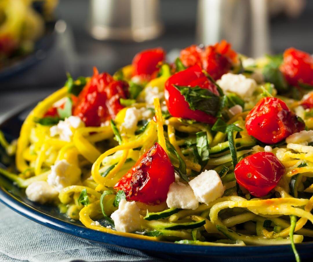 bowl of zucchini pasta topped with fresh tomatoes