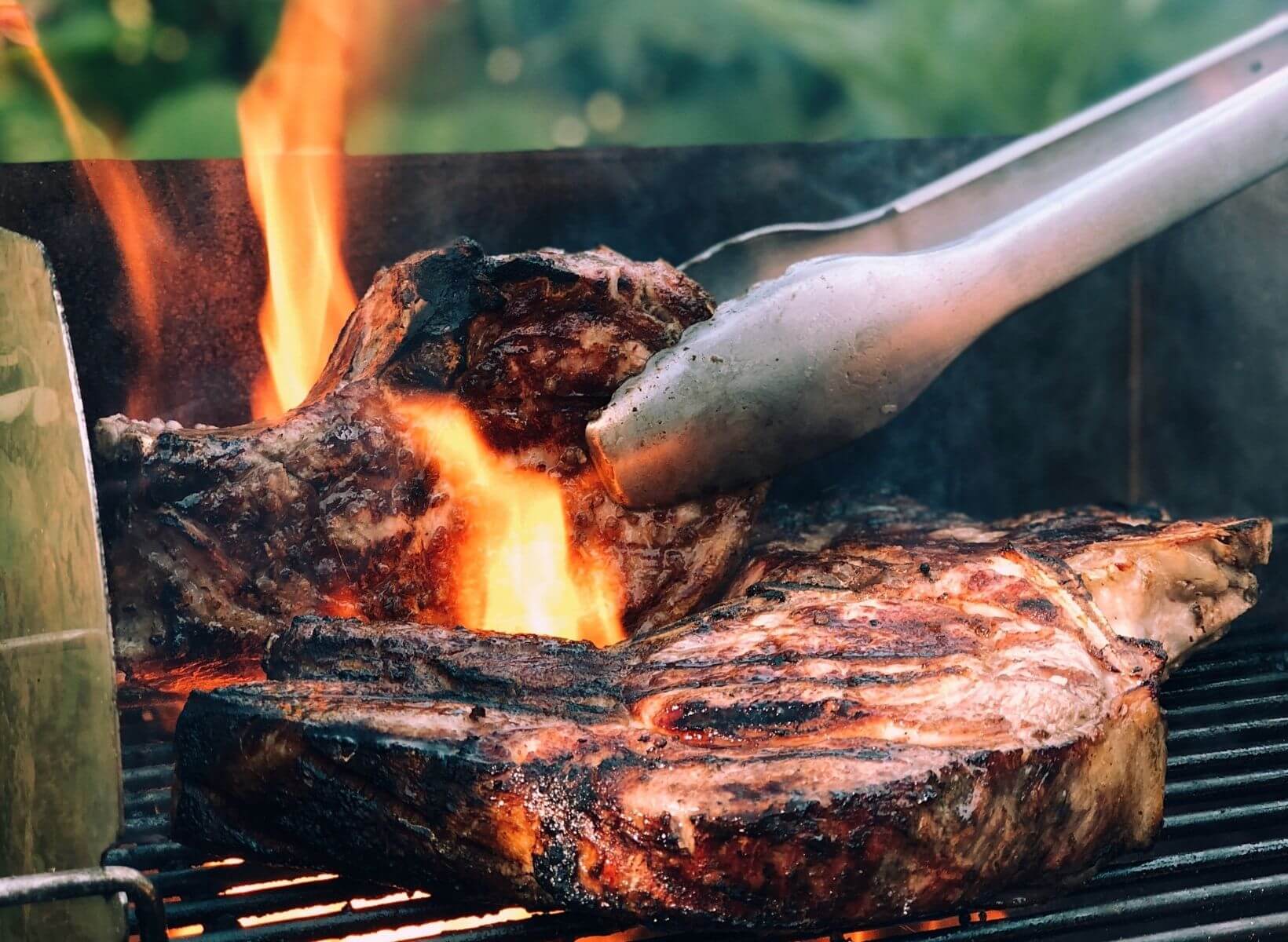 Close up shot of tongs turning steak on grill grates