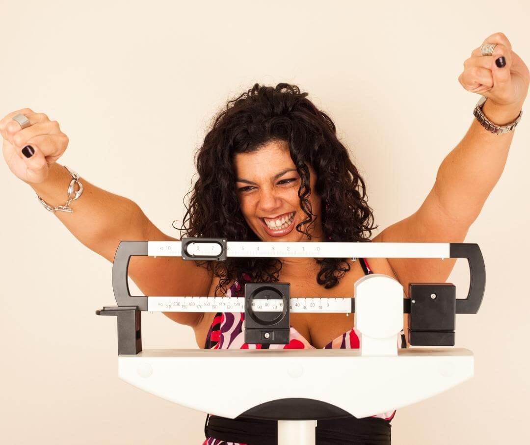 smiling woman standing on a scale with arms in victory pose