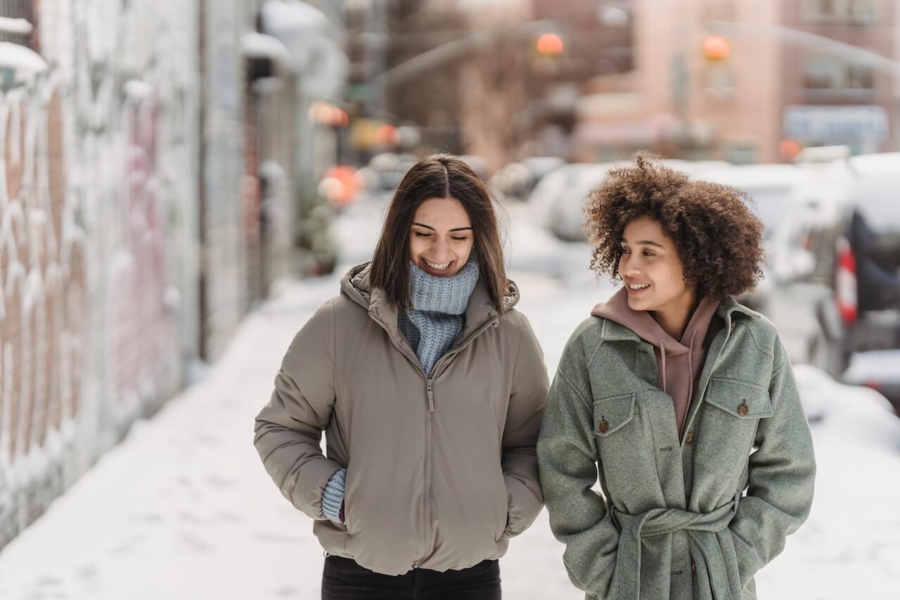 Diverse-women-laughing-and-walking-on-snowy-sidewalk