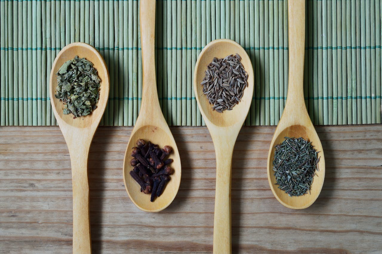 brown-wooden-spoon-with-herbs-on-top-of-green-bamboo-mat-and-brown-wooden-surface-